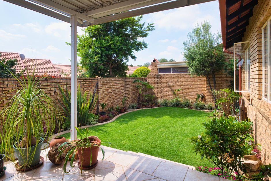 High-resolution photograph of a well-maintained garden in the Bell Green estate, showing a lush green lawn with freshly mowed grass bordered by neatly trimmed hedges and flower beds filled with colorf